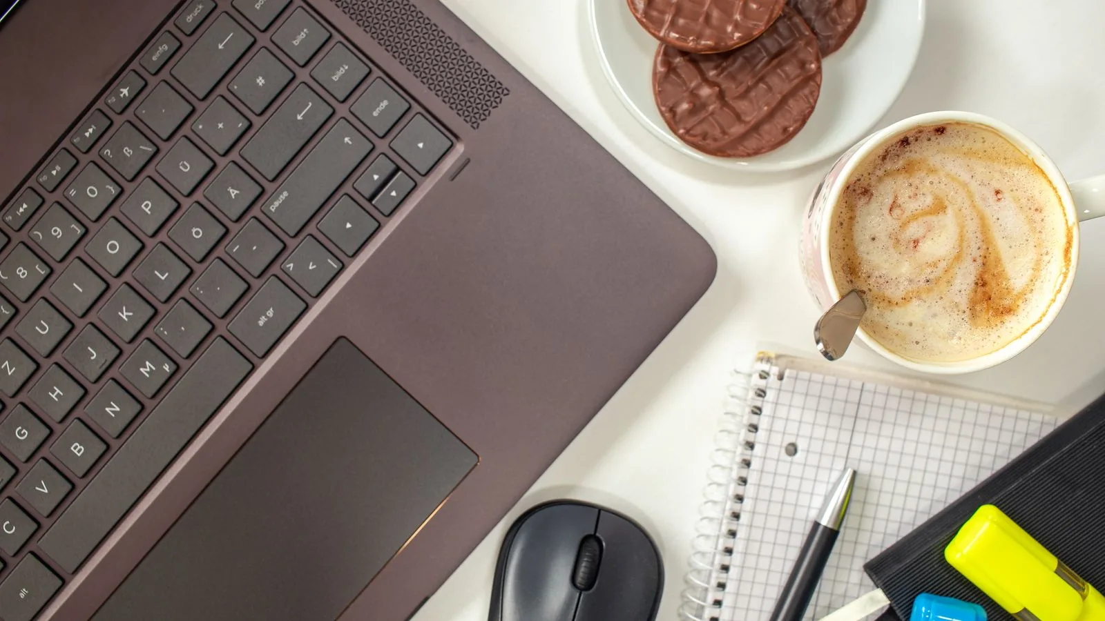 Teclado de notebook ao lado de biscoitos e xícara de café