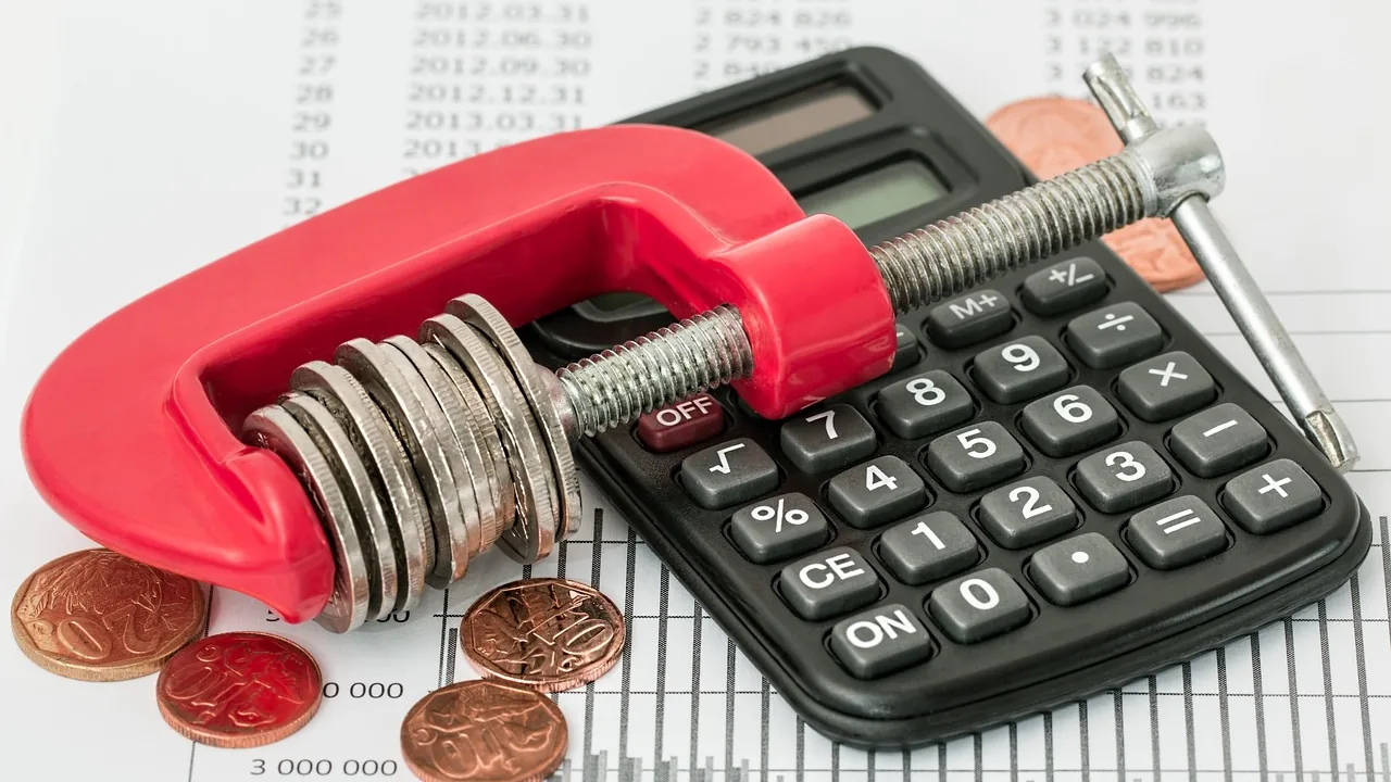 Calculadora e moedas presas em um grampo vermelho, representando a pressão de uma dívida