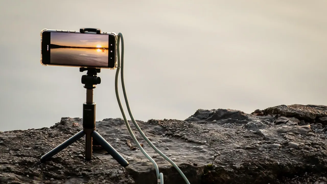 Celular em tripé gravando o pôr do sol, representando a produção de conteúdo por influenciadores digitais