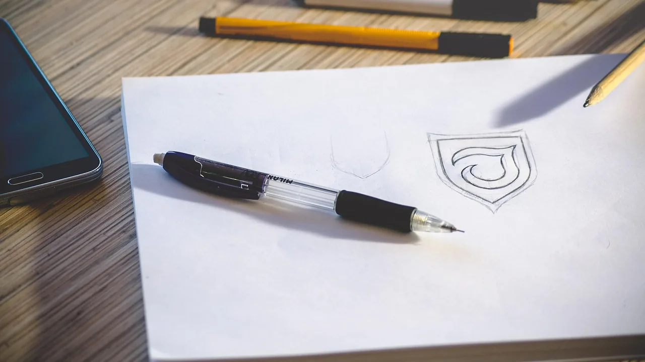 Esboço de logotipo desenhado a lápis em folha branca sobre mesa de trabalho