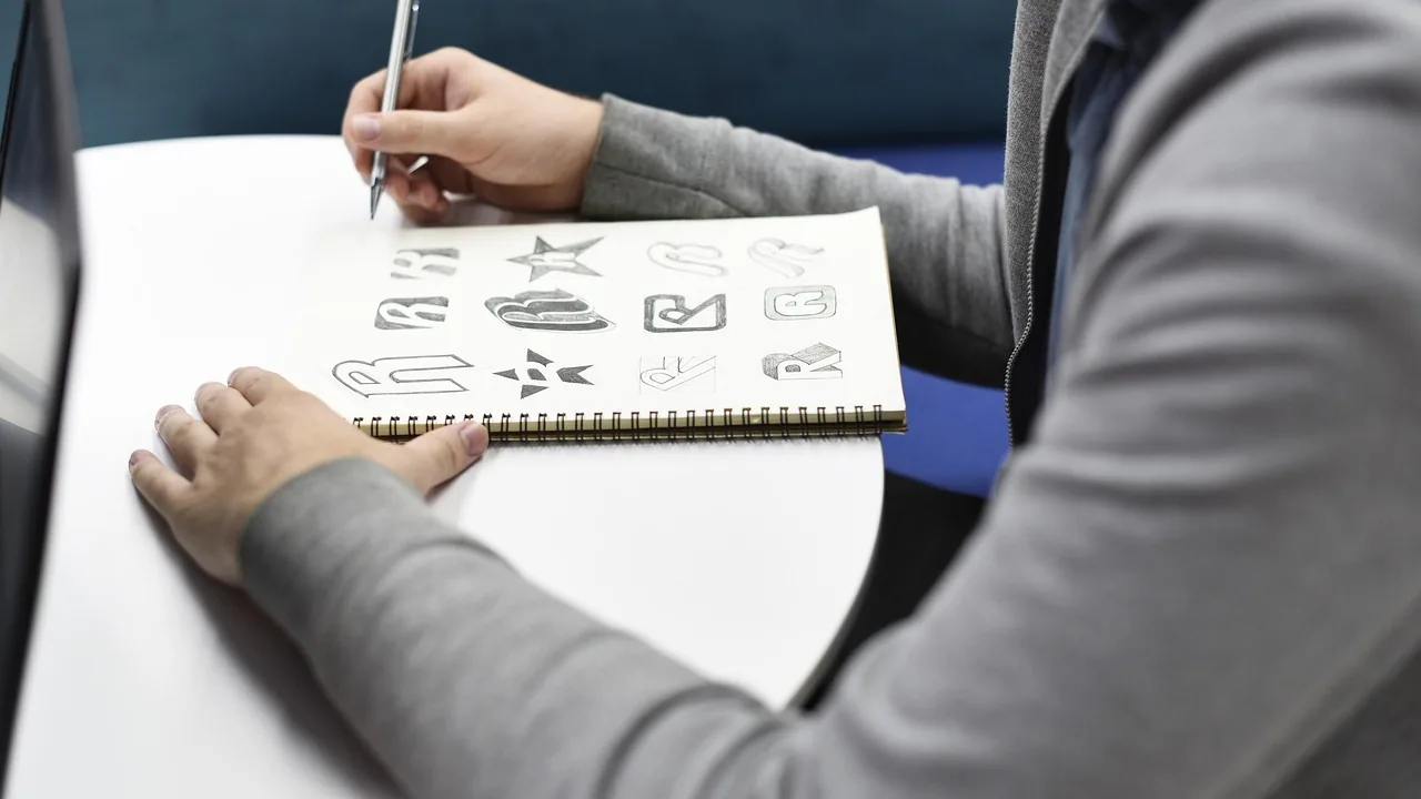 Mão desenhando esboços de ícones e logotipos em caderno