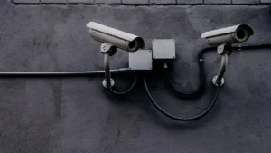 Duas câmeras de vigilância presas a uma parede escura, representando os limites do monitoramento e a privacidade