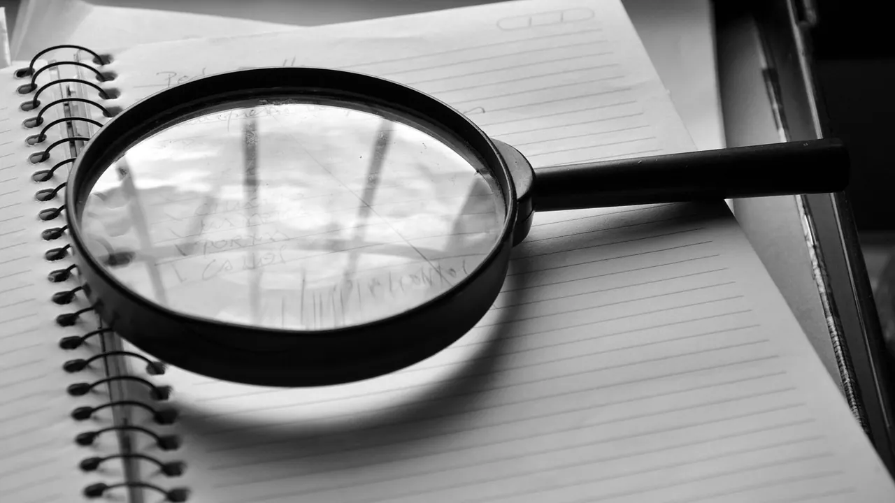 Registro de marca: 5 erros que levam ao indeferimento 3 Lupa sobre um caderno aberto, representando a busca prévia de anterioridade antes do pedido de registro de marca