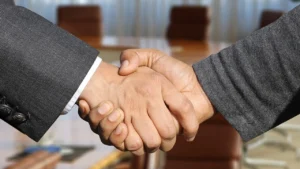 Aperto de mão entre duas pessoas em sala de reunião, representando a confiança entre contratantes