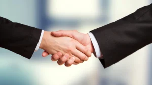 Aperto de mão entre dois executivos de terno, representando o acordo de licença de uso de marca