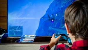 Criança de costas jogando videogame em frente à televisão, representando jogos usados por menores
