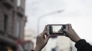 Mãos segurando celular para fotografar uma rua, representando fotos feitas e compartilhadas pelo celular